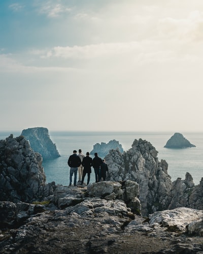 五个人站在岩石山上观看平静的大海